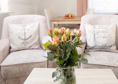 Unterkunft auf Baltrum: Sessel mit maritimen Kissen und einem Strauß mit Rosen