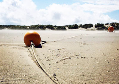 Zwei orangene Bojen am Strand die leicht vom Wind verweht sind